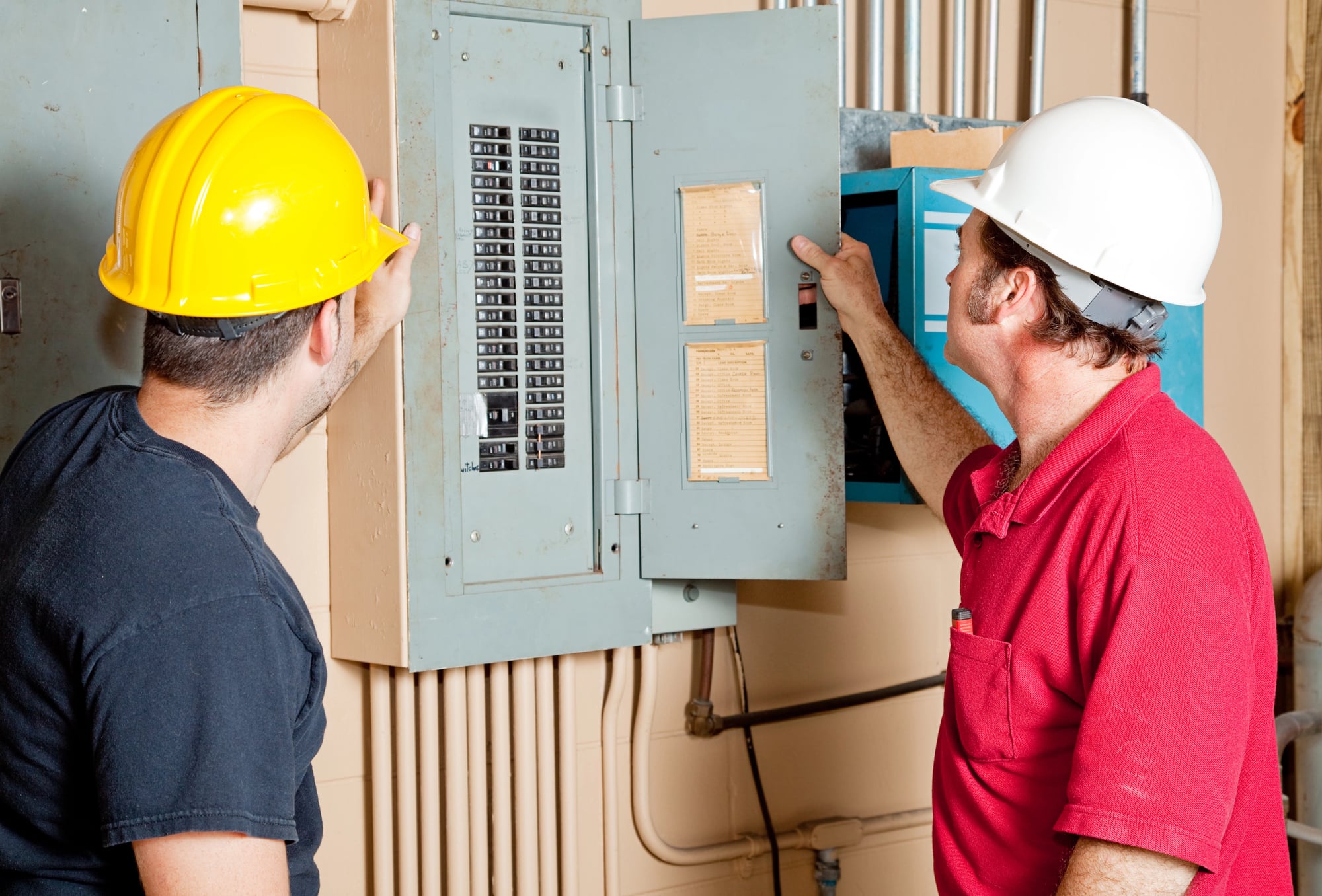 Two electricians in hard hats examining an open residential electrical panel and its handwritten circuit directory