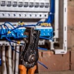 Wire stripping tool positioned in front of electrical panel with blue cables