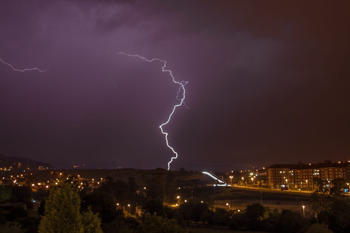 A lightning bolt striking down over a lit city skyline during a night-time thunderstorm