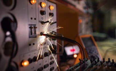 Bright dangerous electronic sparks of current quickly and sharply scatter from an unsafe short circuit on complex technological equipment, in a dark room with electrical appliances