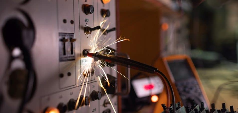 Bright dangerous electronic sparks of current quickly and sharply scatter from an unsafe short circuit on complex technological equipment, in a dark room with electrical appliances