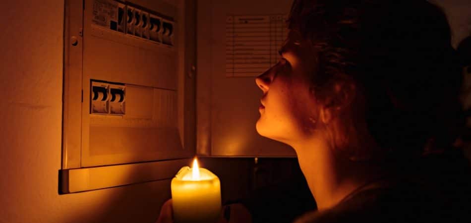young woman with candles in complete darkness examines fuse box or electrical distribution board at home during power outage. Blackout, no electricity