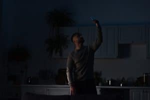 man holding smartphone in raised hand while searching for connection during energy blackout