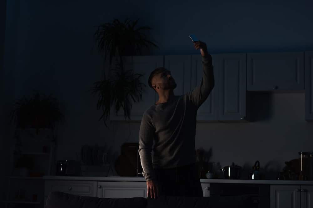 man holding smartphone in raised hand while searching for connection during energy blackout