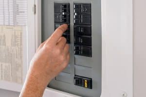 Woman's hand operating a residential electrical panel inside a home. Concept of household electricity, power control, safety, maintenance, and home utilities in a domestic interior